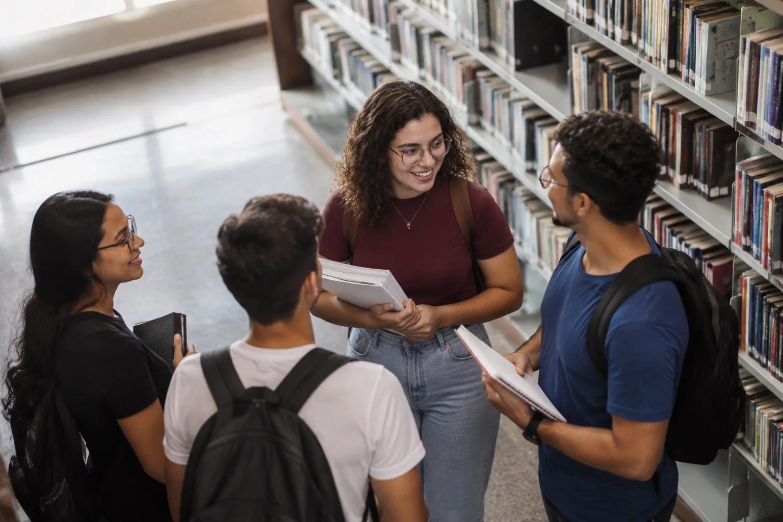 Estudantes conversando em pé entre as estantes de uma biblioteca